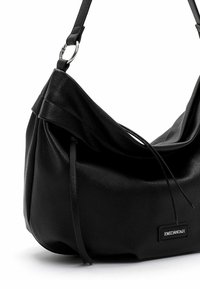 Black leather shoulder bag with a soft, slouchy design. Features a thin adjustable strap and a logo patch. Textured surface with drawstring detail.