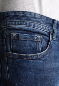 Jeans i denim med en mörkblå färg, klassisk femficksdesign och synliga sömnadsdetaljer samt en liten myntficka på höger sida.