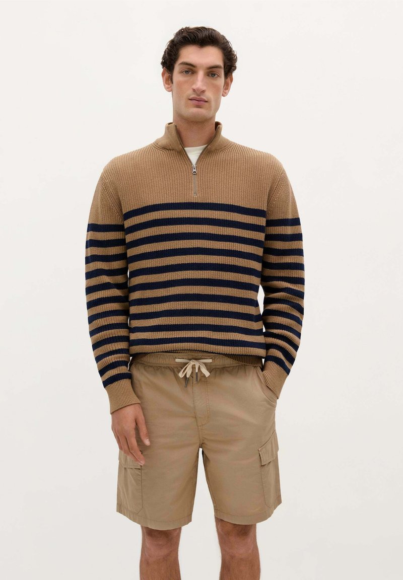 Brun og marineblå stribet sweater med høj krave og lynlås, parret med beige cargo shorts med sidelommer og elastisk talje med snor.