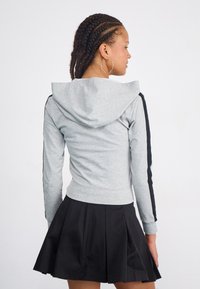 Hanorac gri deschis cu o dâra neagră pe mâneci și o buzunar tip cangur, purtat deasupra unei fuste plisate negre. Material moale, design casual.
