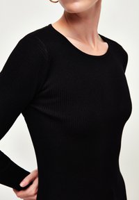 Schwarzes, geripptes Langarmoberteil mit Rundhalsausschnitt, das eine taillierte Silhouette und eine glatte Textur aufweist. Akzente umfassen ein dünnes, langgezogenes Design.