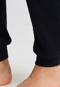 Navy blue cotton pants with a tapered design, featuring an elastic cuff at the ankle. Smooth texture and relaxed fit.