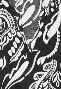 Blusa di tessuto nero con un motivo floreale e paisley bianco, scollatura a V e una superficie morbida e texturizzata.