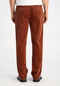 Pantalones marrones de pana con costillas verticales, que cuentan con bolsillos traseros con herrajes plateados. Diseño de pierna recta con textura suave.