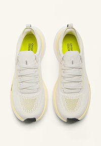 Fehér sportcipők, légáteresztő hálós felsőrésszel, texturált részletekkel és sárga-zöld béléssel, könnyű talppal és felhúzófüllel.