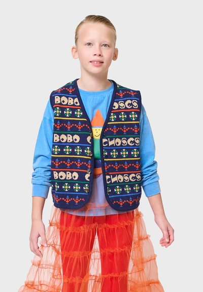 Mörkblå stickad väst med färgglada mönster och texten "BOBO CHOSES," tillsammans med en ljusblå långärmad tröja och en orange tutu-kjol.