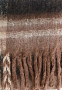 Fodera in lana a quadri marrone e crema con frange, caratterizzata da una texture morbida e motivi con diverse tonalità di marrone e grigio.