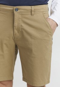 Bermudy khaki wykonane z mieszanki bawełny, z zapięciem na guzik, dwoma bocznymi kieszeniami oraz widocznymi detalami przeszycia. Gładka tekstura.