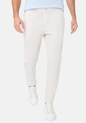 Light beige trousers with a smooth texture, tapered fit, front pleats, and side pockets, paired with white sneakers for a casual look.