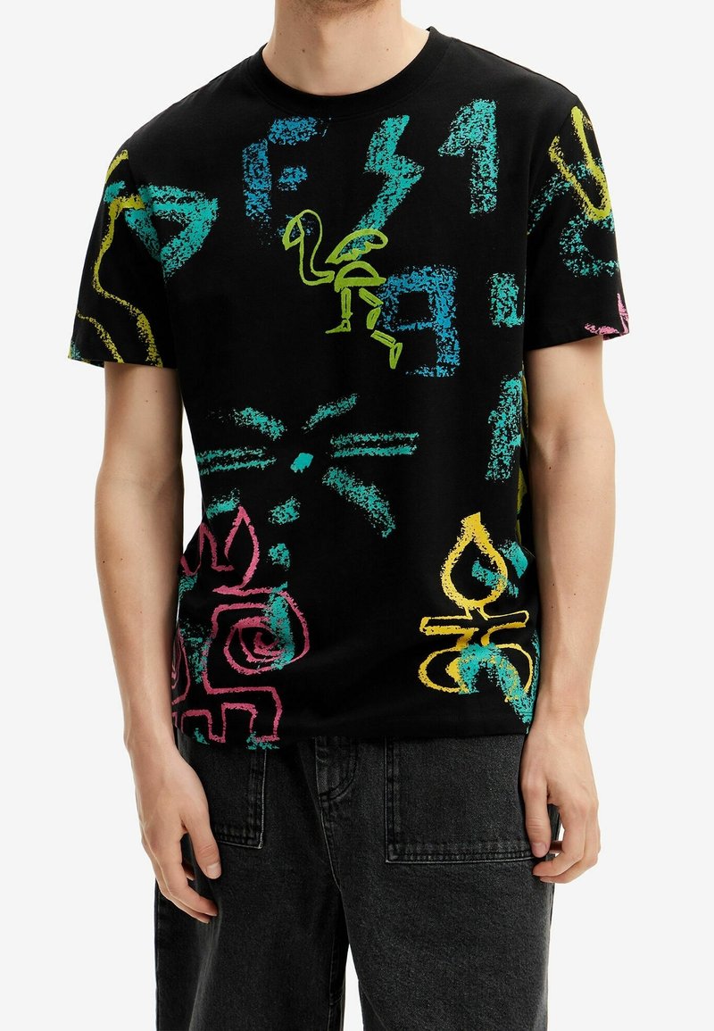 T-shirt en coton noir avec des motifs colorés et abstraits de style graffiti en vert, rose et bleu. Manches courtes, design à col rond.