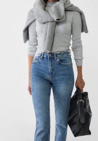 Grå rippad tröja över axlarna, högmidjade blå jeans och en svart läderväska med ett metallhandtag. Mjuka texturer och avslappnad design.