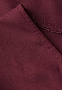 Tissu bordeaux avec une texture lisse, présentant un bord replié et des coutures visibles. Le matériau semble léger et tombe en douceur.