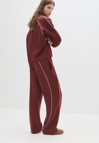 Bordeaux sweatshirt og matchende brede bukser med hvide piping-detaljer, lavet af et blødt stof, stylet til en afslappet pasform.