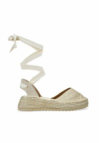 Sandalia de esparto beige con suela de yute trenzado, cinta de tela en el tobillo y diseño de punta abierta. Presenta una parte superior texturizada y un acento en el talón con patrón de cuadrícula.