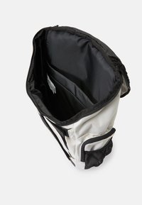 Saco branco e preto com um fecho de correr, bolso interno e um bolso lateral de malha. O interior é liso e preto, projetado para armazenamento.