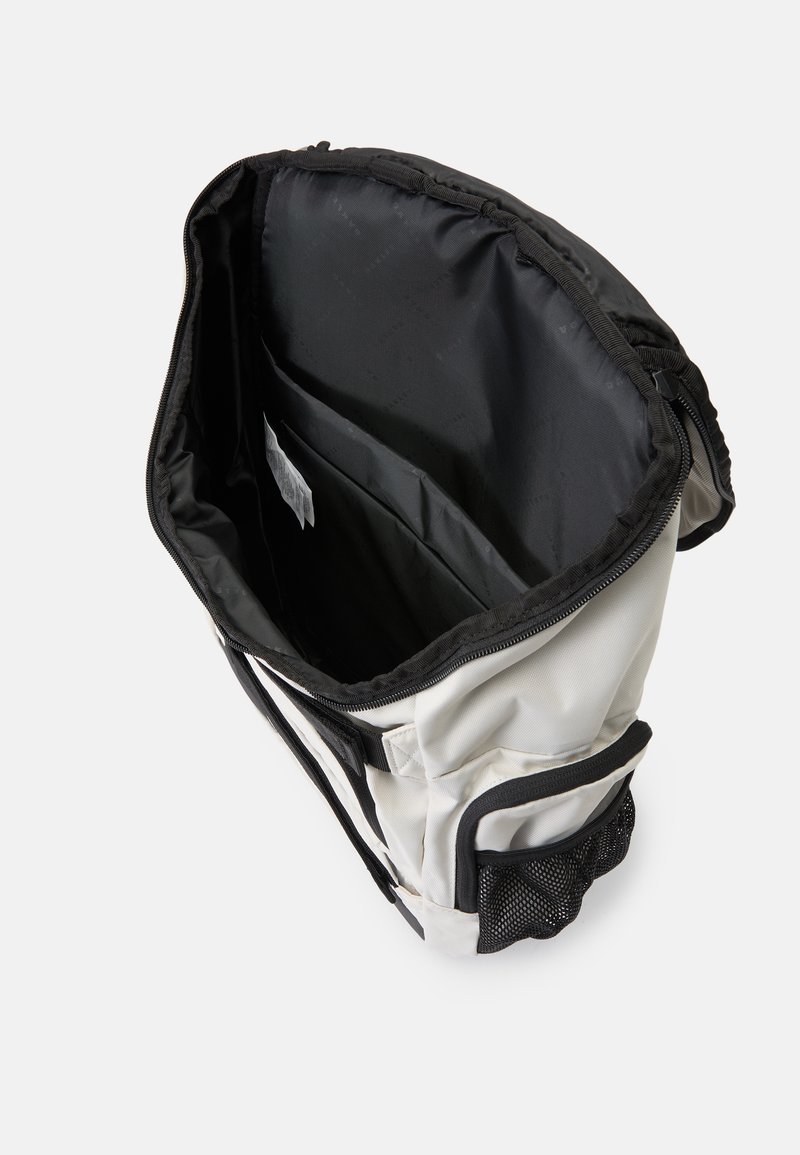 White and black bag with a zippered opening, internal pocket, and a mesh side pocket. The interior is smooth and black, designed for storage.