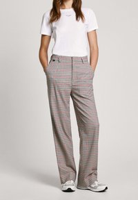 Bílá tričko s modrým logem, šedé kostkované kalhoty s červenými a černými akcenty, volný střih, boční kapsy, spárováno se šedými teniskami.