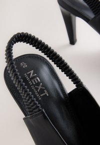 Sandali con tacco neri in morbida pelle, caratterizzati da un cinturino testurizzato e una punta affusolata elegante. Logo argentato sulla soletta. Taglia 40.