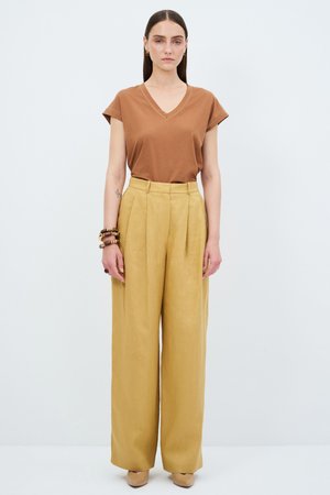 Bruine v-hals t-shirt, korte mouwen, gecombineerd met hoge taille, wijdvallende, mosterdgele broek. Accessoires omvatten een multi-bangle armband.