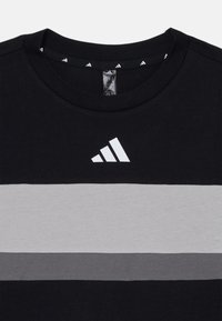 Svart bomull T-skjorte med grå horisontale striper og hvit Adidas-logo på brystet. Rund hals og ribbet krage.