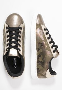 Czarne sneakersy na sznurówki z metalicznymi złotymi akcentami, płóciennymi w kolorze moro, wyściełanym kołnierzem i białą gumową podeszwą. Logo marki widoczne w środku.