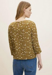 Bluse in Braun mit floralem Muster, 3/4-Ärmeln, Rückenausschnitt und lässiger Passform. Kombiniert mit blauen Jeans.