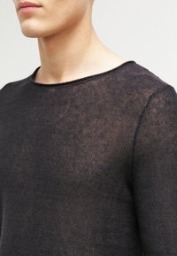 Černý, lehký pletený svetr s kulatým výstřihem a texturovanou tkaninou. Design má mírně volný střih a viditelné švy.