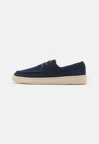 Zapatos sin cordones de ante azul marino con puntera redonda y cordones elásticos. Suela de goma de color crema con un agarre texturizado y detalles de costura alrededor de los bordes.