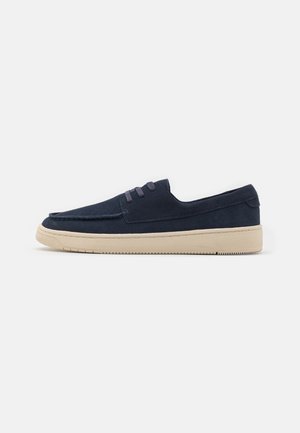 Zapatos sin cordones de ante azul marino con puntera redonda y cordones elásticos. Suela de goma de color crema con un agarre texturizado y detalles de costura alrededor de los bordes.
