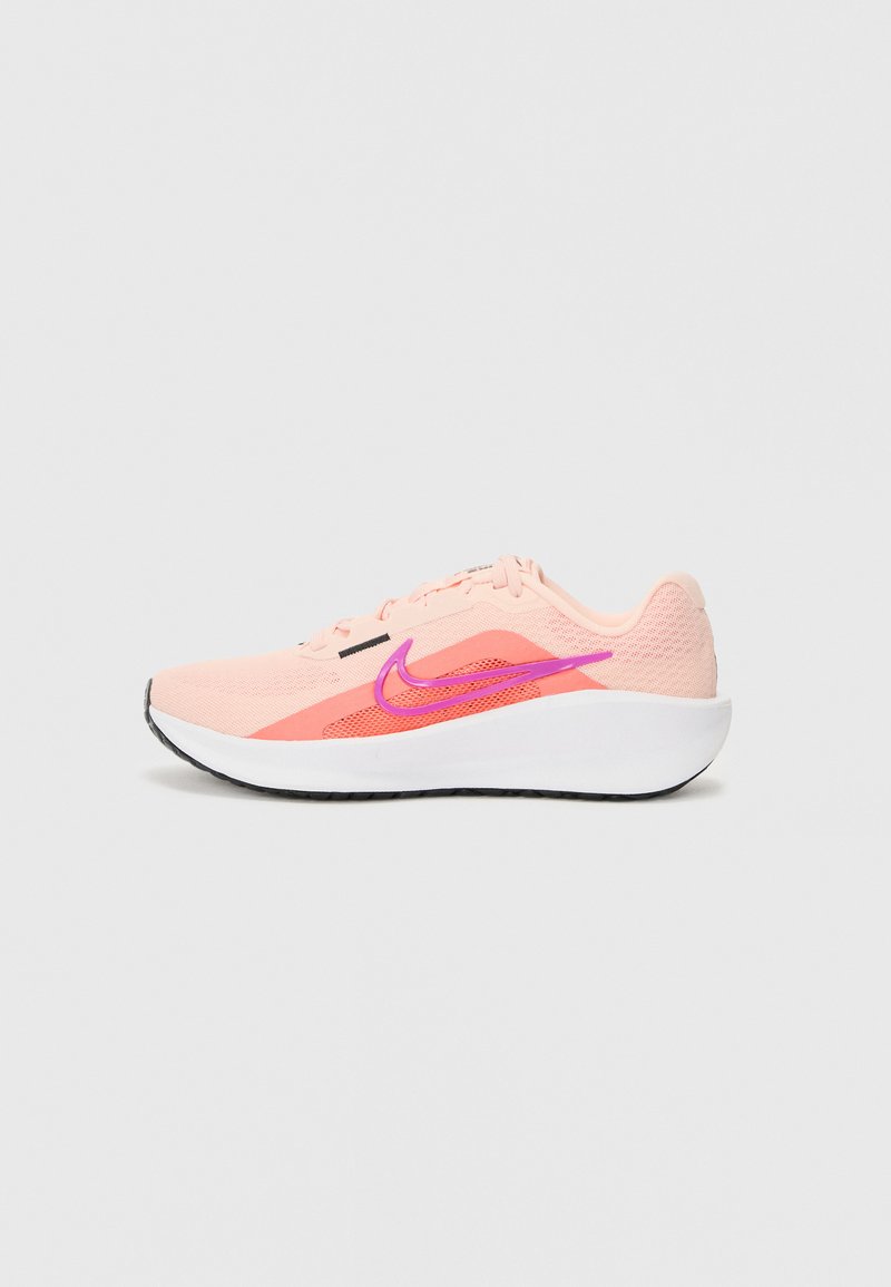 Sapatilha desportiva rosa clara com uma parte superior de malha respirável, um swoosh roxo em destaque, entresola branca e sola de borracha para aderência.