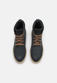 Botas de tobillo de cuero negro con cordones marrones, diseño de punta redonda y superficie texturizada. Cuenta con un cuello acolchado y suelas de goma beige.