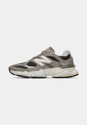 Gray and beige sneaker with a textured upper, featuring mesh and suede panels, a prominent white logo, and a thick, cushioned sole.