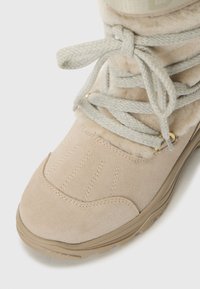 Bézs téli csizma, textúrázott velúrral, bolyhos béléssel és bonyolult fűződésekkel, masszív gumitalppal a tapadás érdekében.