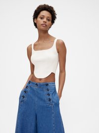 Úzký žebrovaný bílý crop top se čtvercovým výstřihem. Volné modré džíny s vysokým pasem a knoflíkovými detaily po stranách.