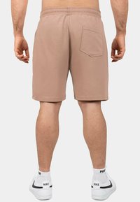 Pantaloni corti in cotone beige con vita elastica, una tasca posteriore e orlo dritto. Abbinati a sneakers bianche e calzini alla caviglia.