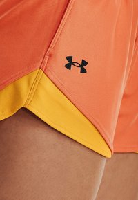 Orange atletshorts med en gul fåll, tillverkade i ett strukturerat tyg och med en svart Under Armour-logotyp på sidan.