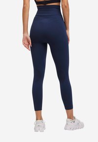 Granatowe legginsy z wysokim stanem, wykonane z elastycznego materiału, z teksturowanymi akcentami i łatami na kolanach. Połączone z białymi butami sportowymi.