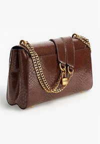 Borsa a tracolla in pelle marrone con texture, dotata di tracolla in catena dorata e chiusura a lucchetto dorato incisa con "GUESS" su uno sfondo bianco.