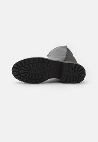 Botte noire imperméable avec une semelle en caoutchouc épaisse et texturée, dotée d'un dessus lisse et de coutures renforcées le long des joints.