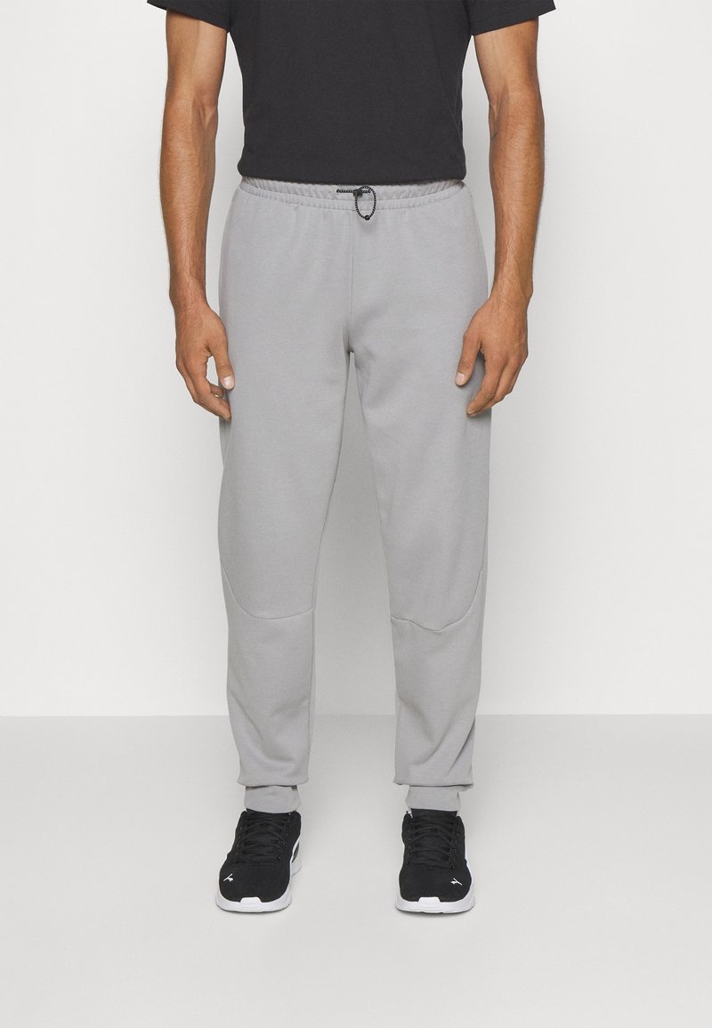 Pantalones de chándal gris claro con cintura ajustable, piernas estrechas y puños acanalados. Combinados con zapatillas deportivas negras.
