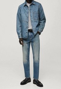 Chaqueta de mezclilla en azul claro con un bolsillo, combinada con jeans de mezclilla azul claro. Camiseta gris debajo, cinturón negro y zapatos negros.