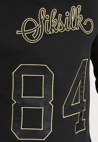 Maglia sportiva nera con logo "Siksilk" ricamato in oro e il numero "84" in un carattere audace con una finitura testurizzata.