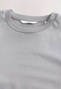 Szürke, pamutból készült, kerek nyakú póló. Sima textúrájú és bordázott nyakrésszel rendelkezik. A címke "NEXT" feliratú.