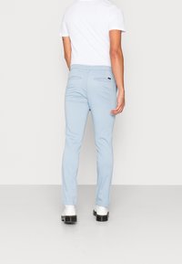 Ljust blå byxor med slim fit, med en jämn yta, bälteshällor och två bakfickor. Bärs tillsammans med en vit t-shirt.