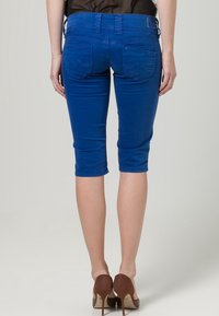 Pantaloni capri in denim blu con un design aderente, vita media e dettagli delle tasche. Texture liscia, che termina appena sotto il ginocchio.