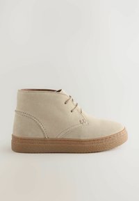 Bottines en cuir suédé beige avec une semelle en caoutchouc texturée, dotées d'un design simple à lacets et d'accents cousus sur la tige.