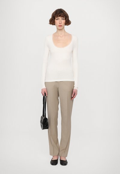 White long-sleeve shirt, beige tailored pants, black flats, holding a black handbag. Simple, fitted design with a scoop neckline and smooth texture.