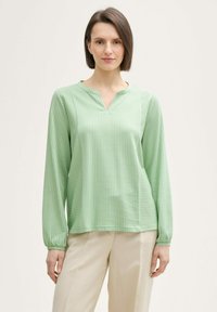 Blouse verte à manches longues avec un col en V, ornée de rayures verticales dans des nuances variées de vert, fabriquée en tissu léger.