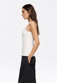Heledbeez tank top õhukeste rihmadega, sile tekstuur ja kehaümbritsev disain, ühendatud laia mustade pükstega. Lihtne ja minimalistlik stiil.