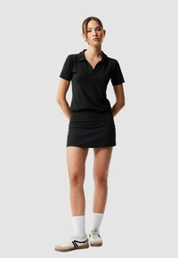 Sort polo skjorte med krave, parret med en matchende sort nederdel. Hvide sportsokker og beige sneakers med sorte detaljer fuldender outfittet.